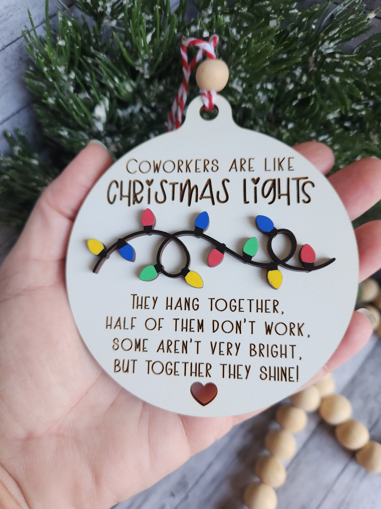 Decorative ornament with Christmas lights design and text, held by a hand with a blurred background.