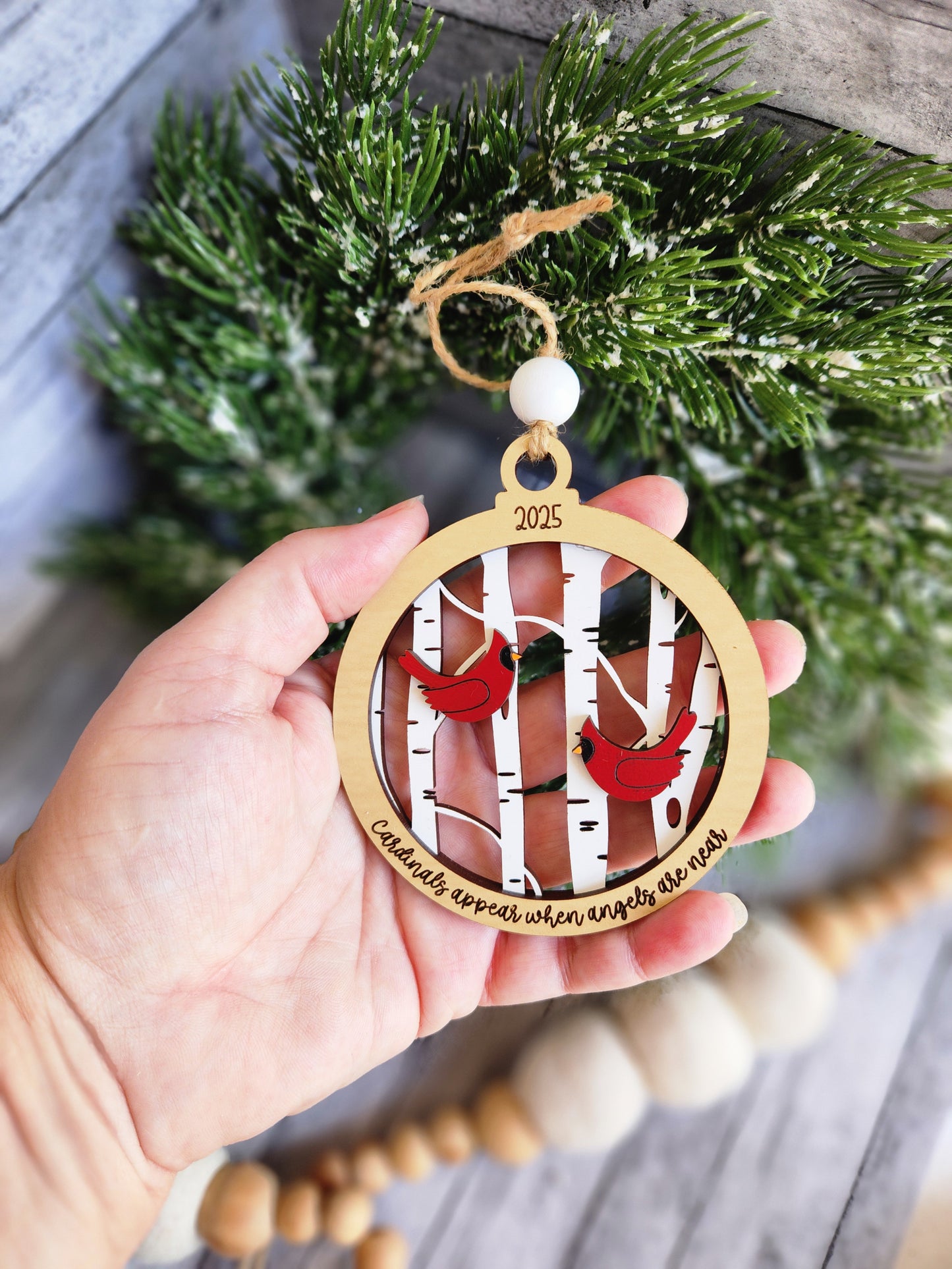 Hand holding a Christmas ornament with a design of a couple and the year 2020, surrounded by festive decorations.