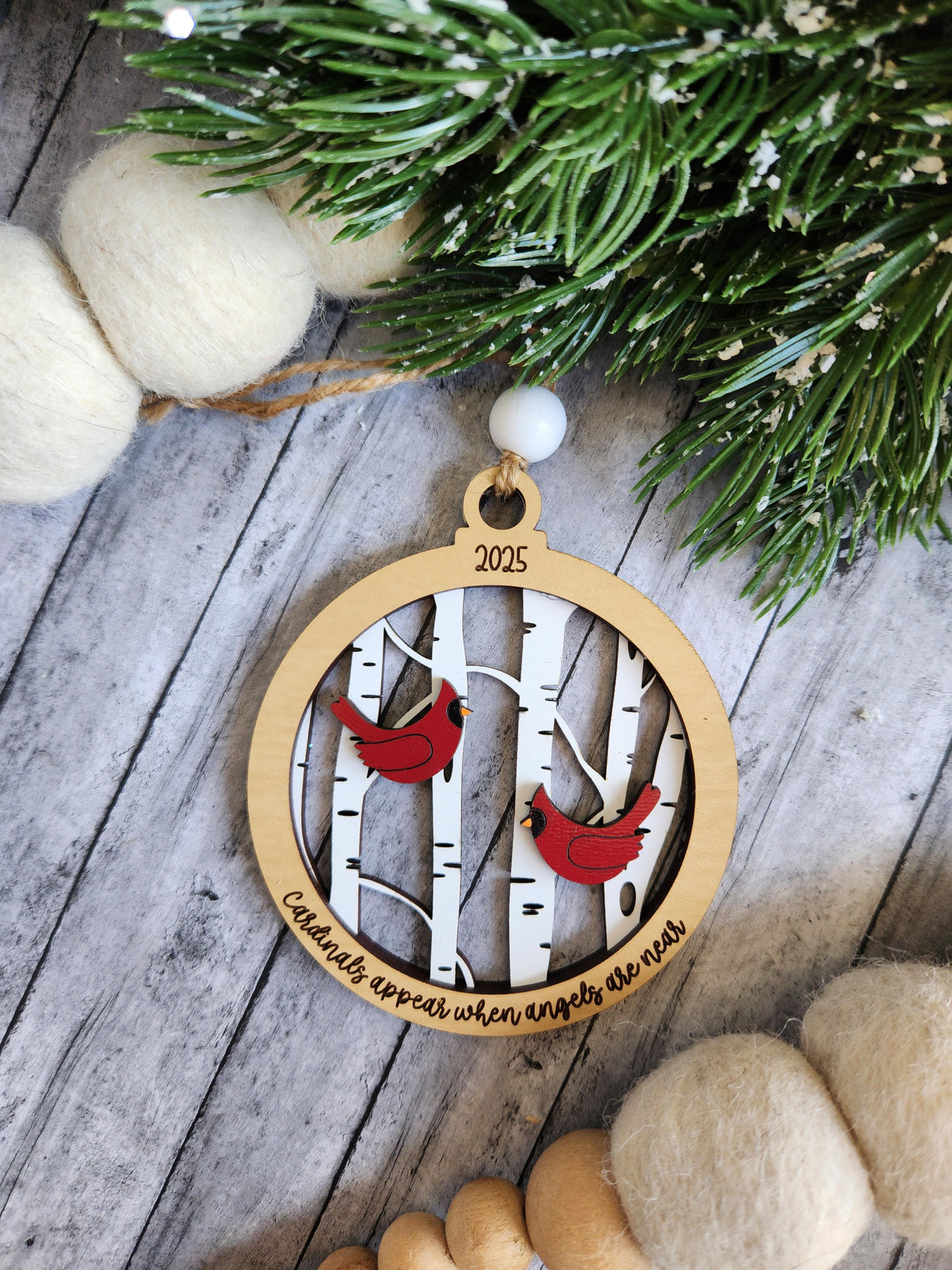 Wooden ornament with red cardinals and birch trees on a rustic wooden surface with greenery.