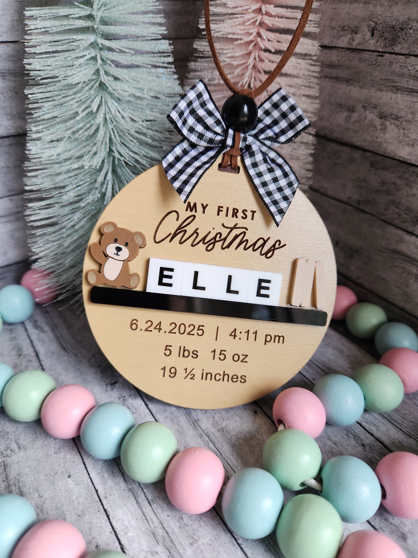 Wooden plaque with baby's first Christmas details, surrounded by colorful beads on a wooden surface.