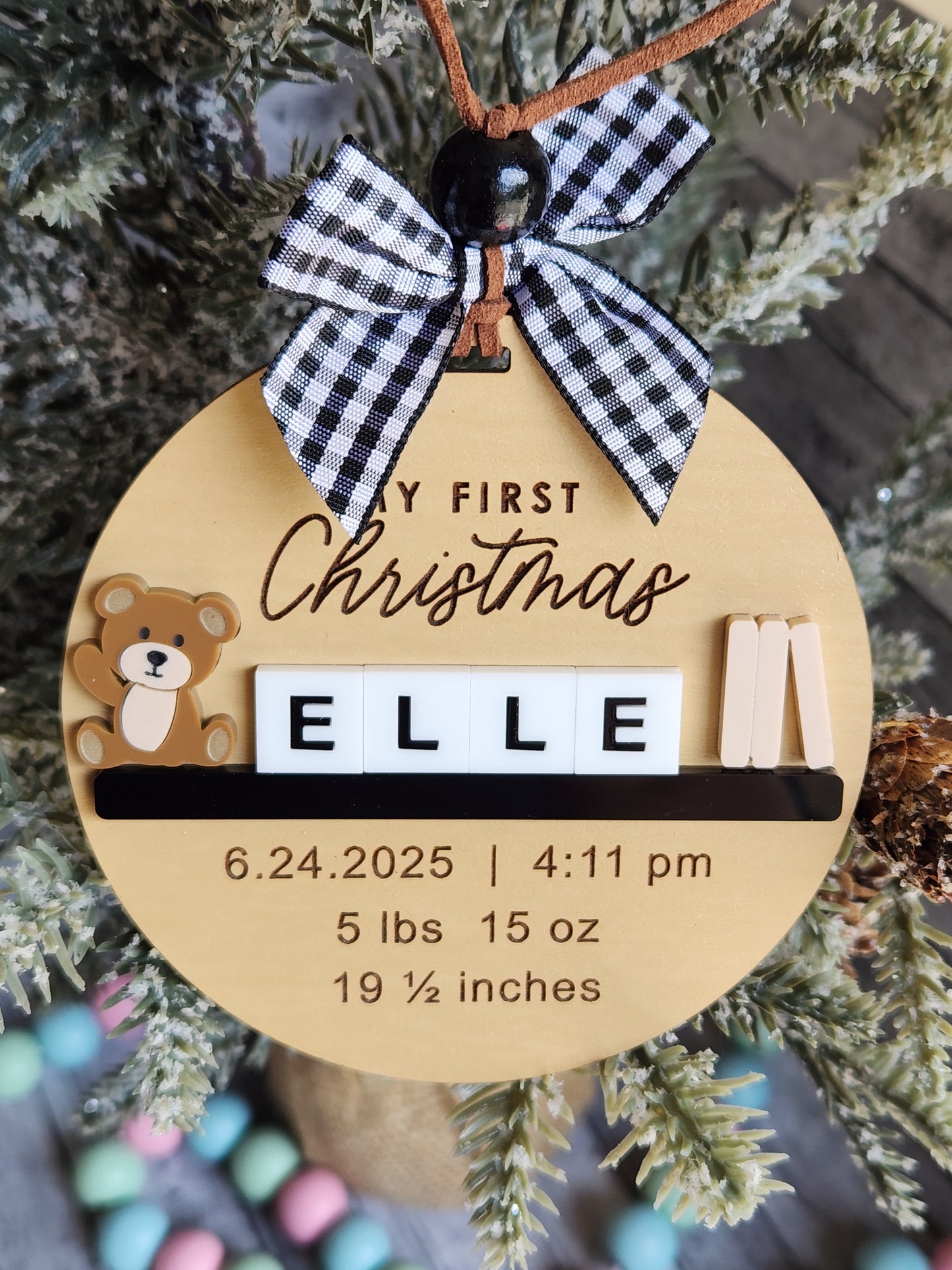 Round wooden ornament with text and a checkered bow, surrounded by Christmas decorations.