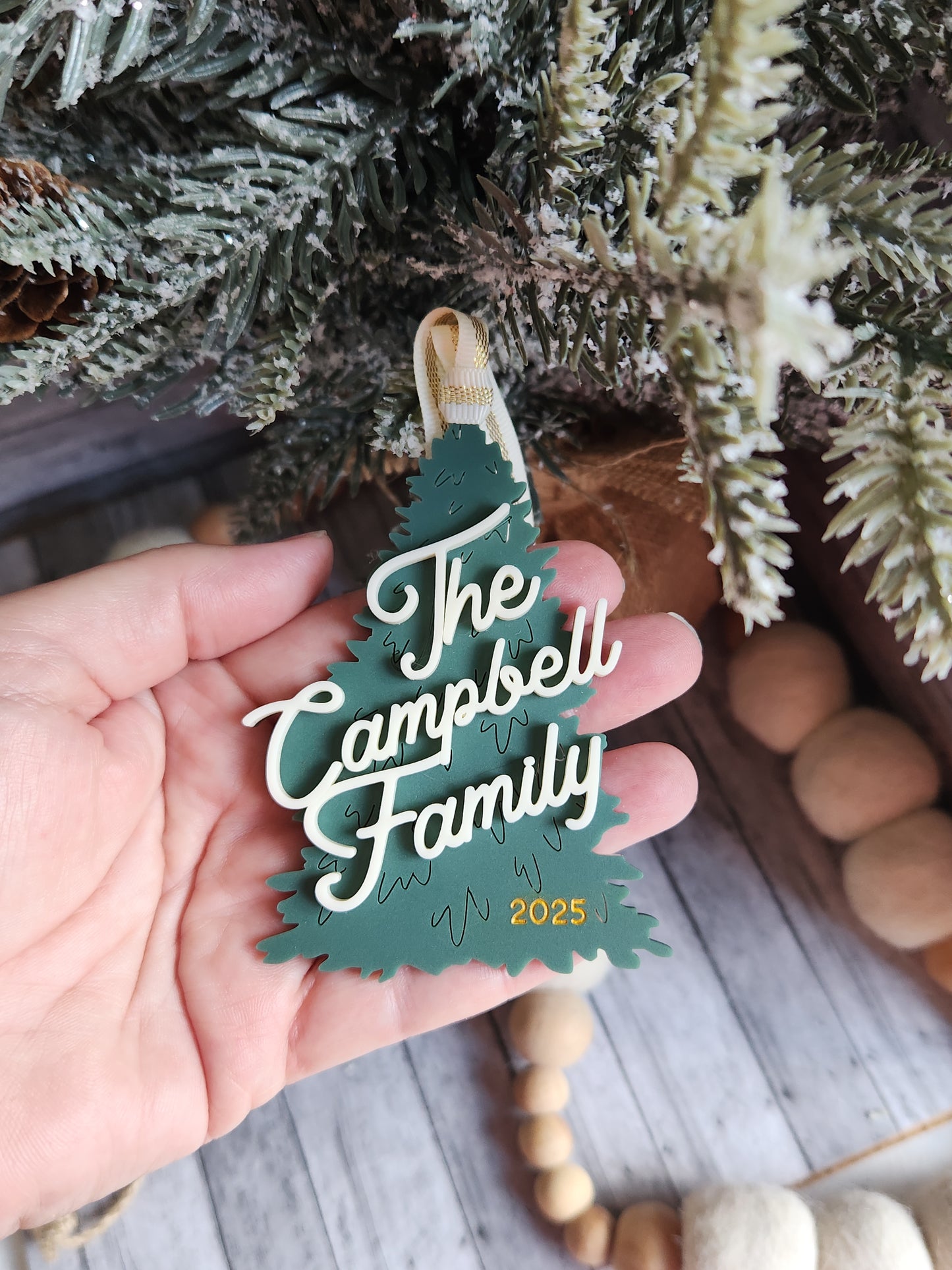 Hand holding a decorative ornament with 'The Campbell Family' text against a festive background.