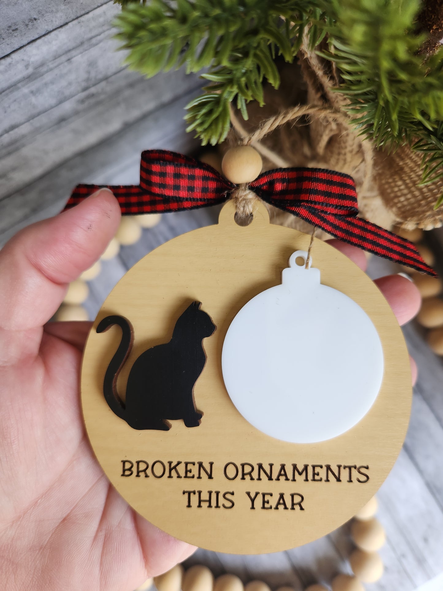 Wooden ornament with a black cat silhouette and text 'Broken Ornaments This Year' held by a hand.