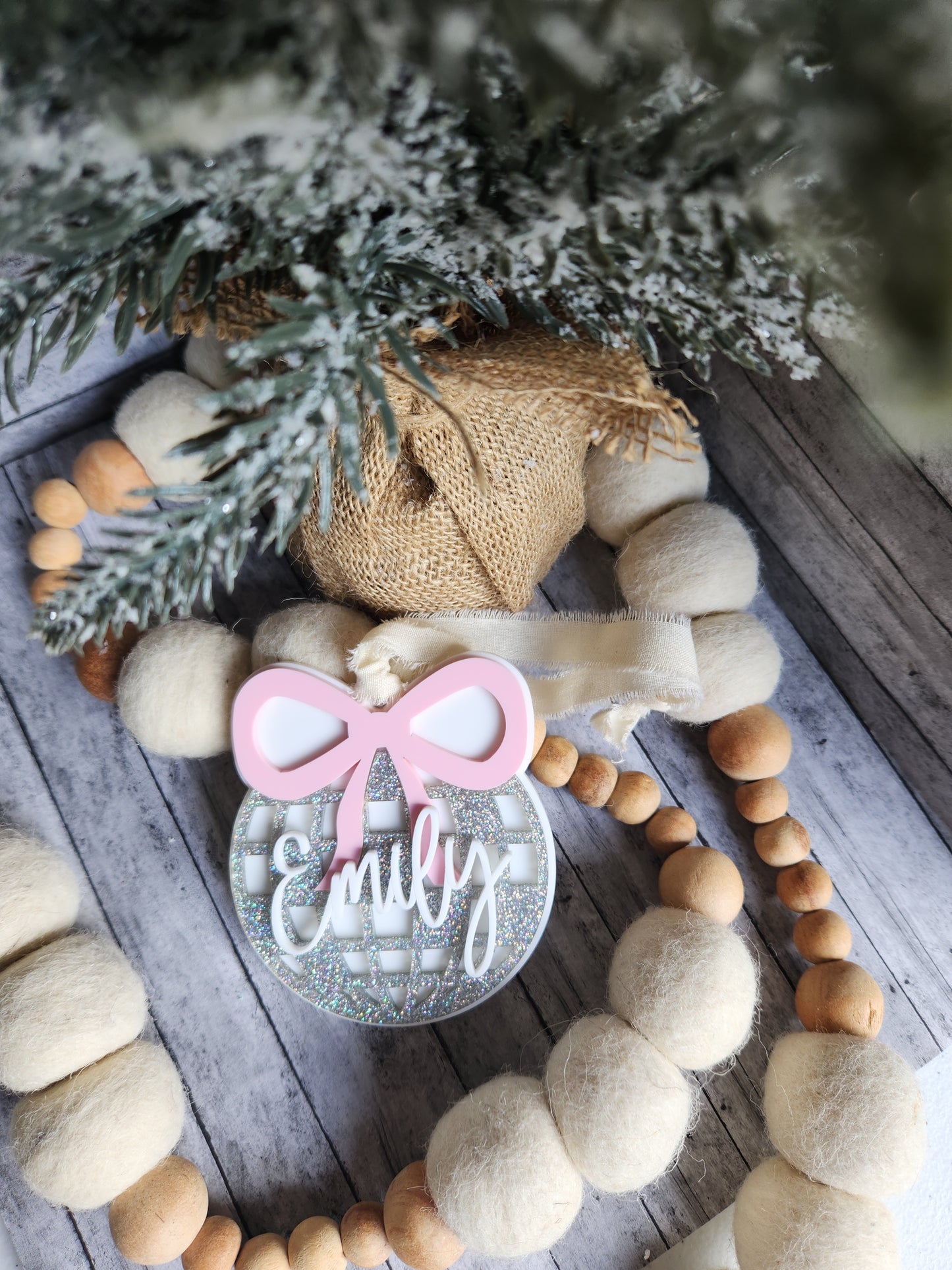 Decorative wreath with wooden beads, burlap fabric, and a pink bow on a wooden surface.