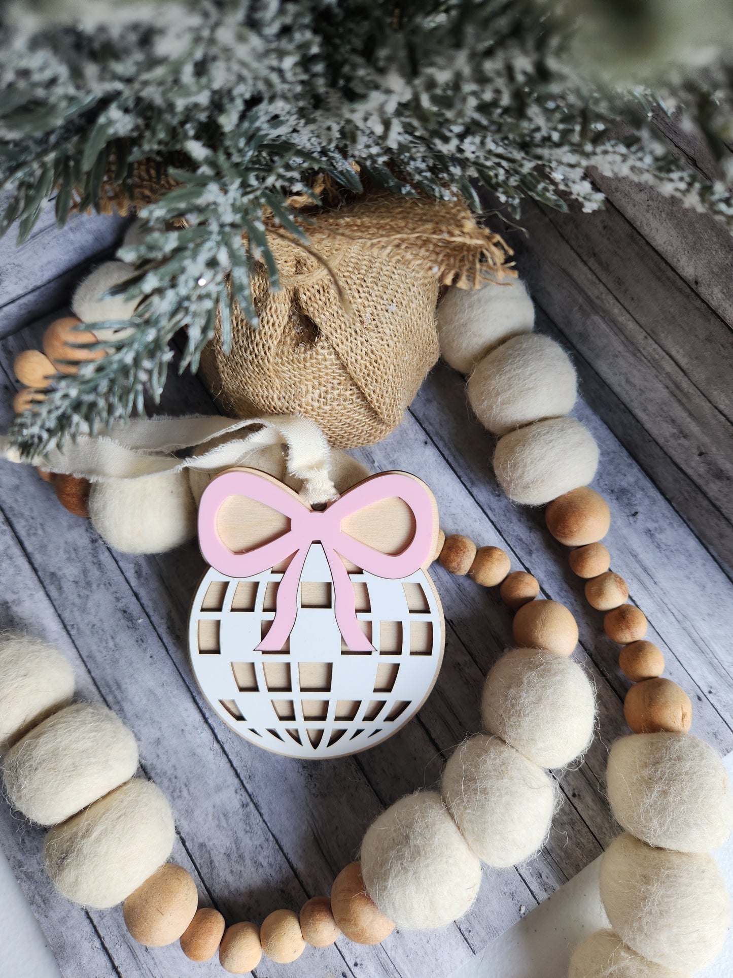 Decorative wreath with wooden beads, burlap fabric, and a pink and white center on a wooden surface.
