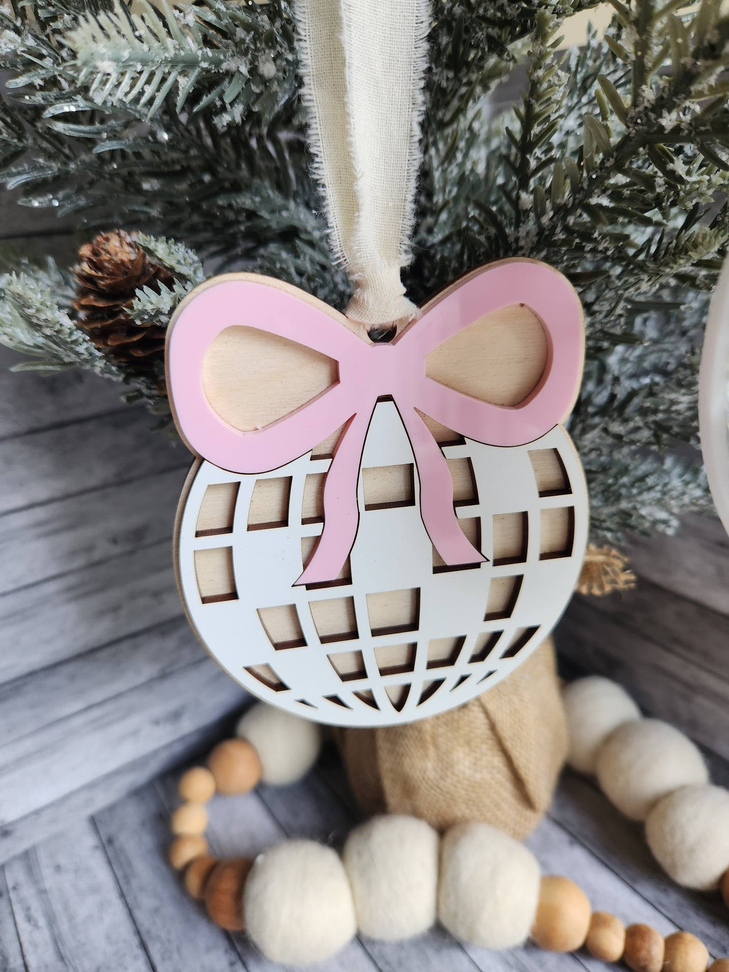 Decorative item with pink ribbon and lattice design on a wooden surface with Christmas tree and beads.