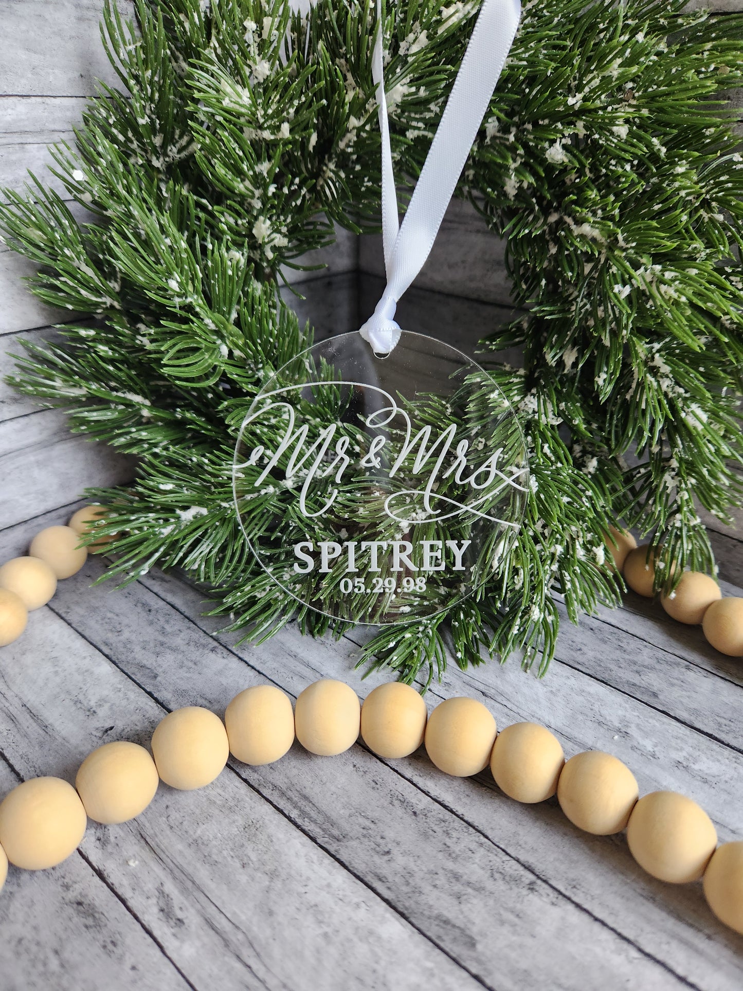 Green wreath with 'Mr. & Mrs.' text, wooden beads on a rustic wooden surface.