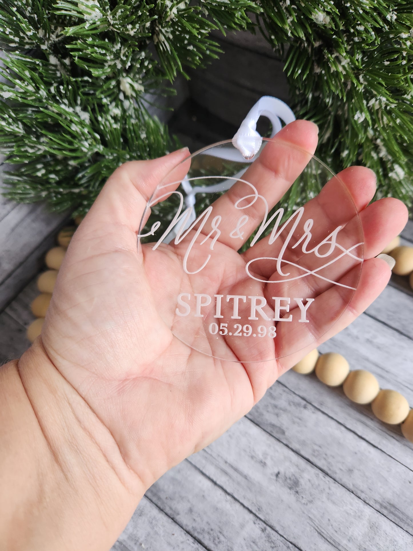 Hand holding a clear ornament with engraved text against a Christmas-themed background