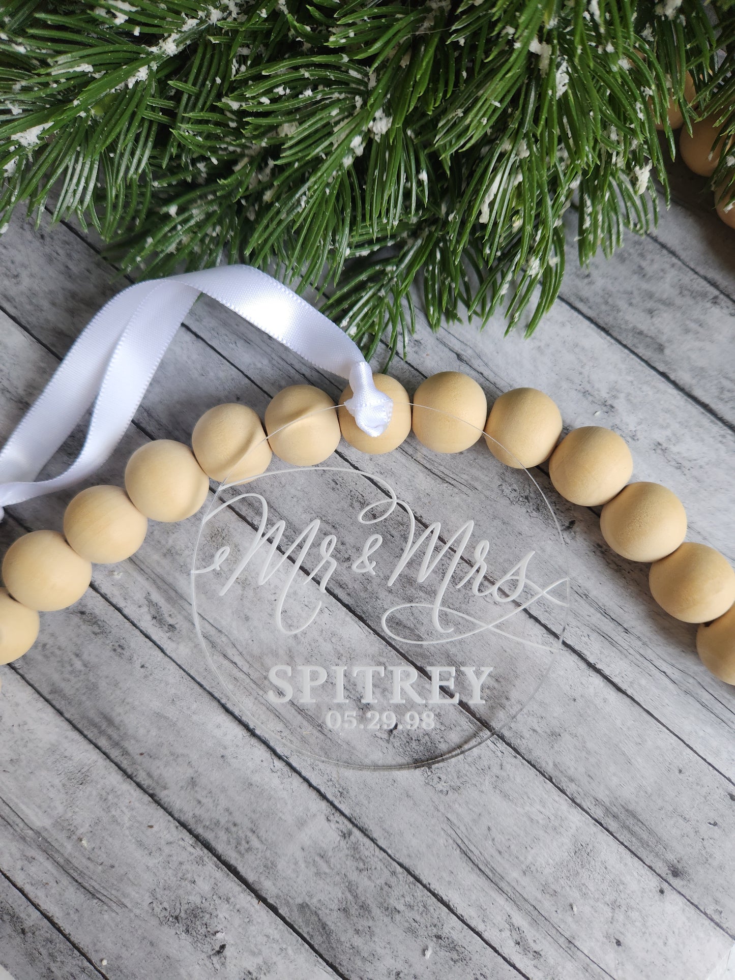Wooden bead garland with a white ribbon on a wooden surface next to a Christmas tree.