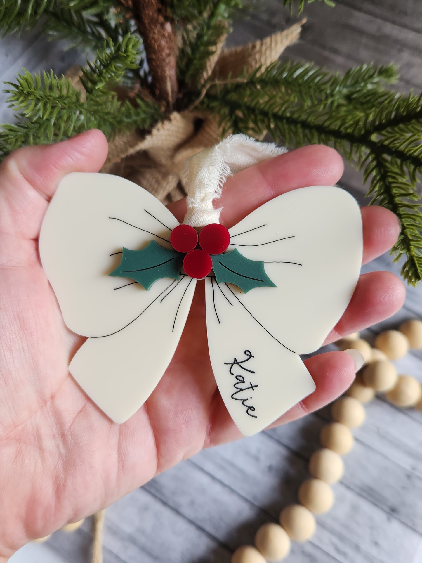 Hand holding a decorative bow with a name tag labeled 'Katie' against a rustic background.