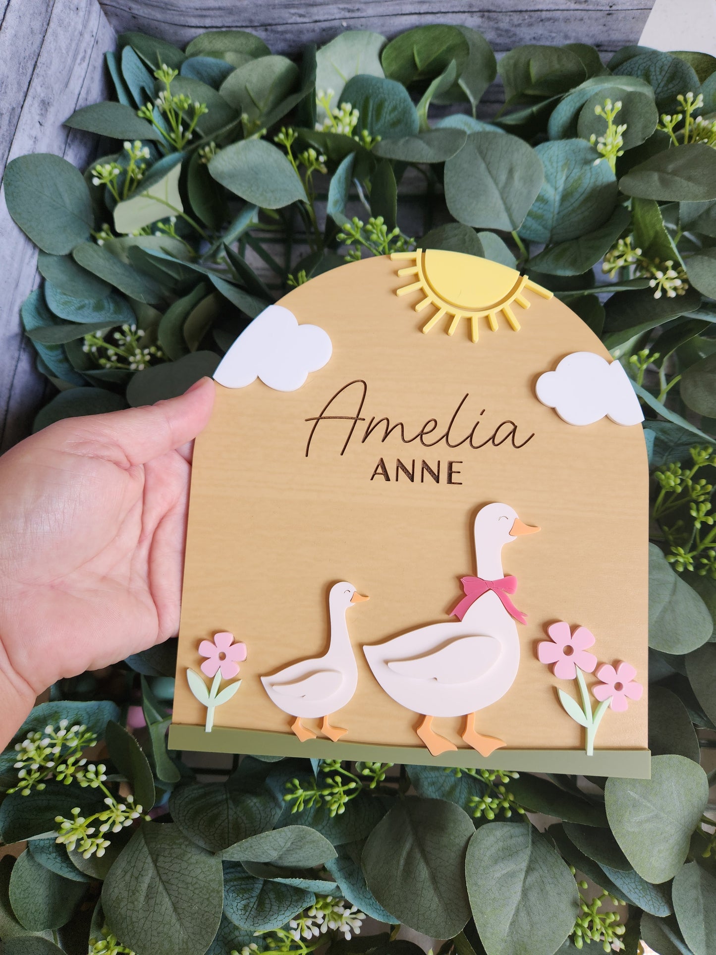 Hand holding a personalized card with decorative elements on a leafy background