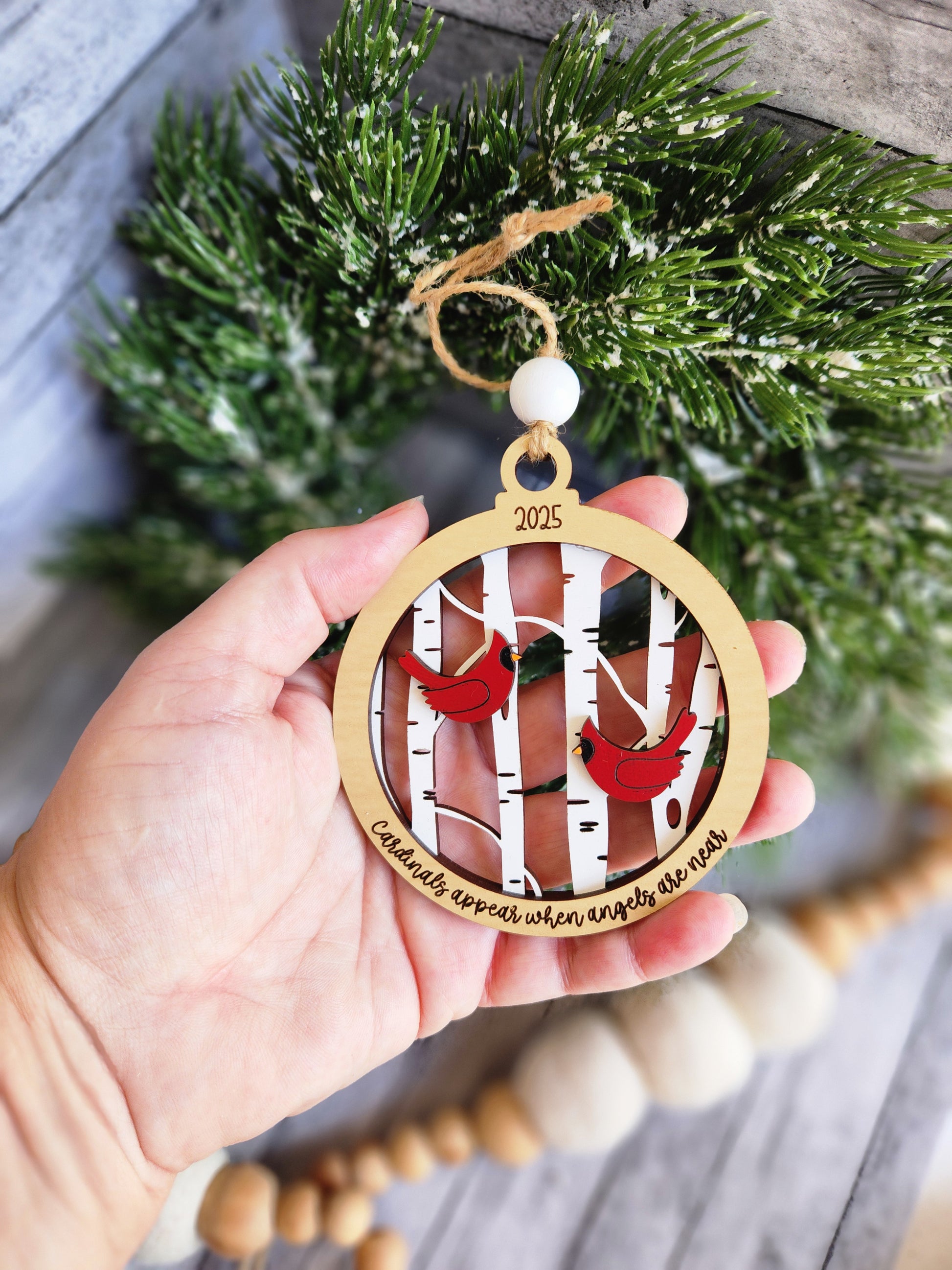 Hand holding a Christmas ornament with a design of a couple and the year 2020, surrounded by festive decorations.