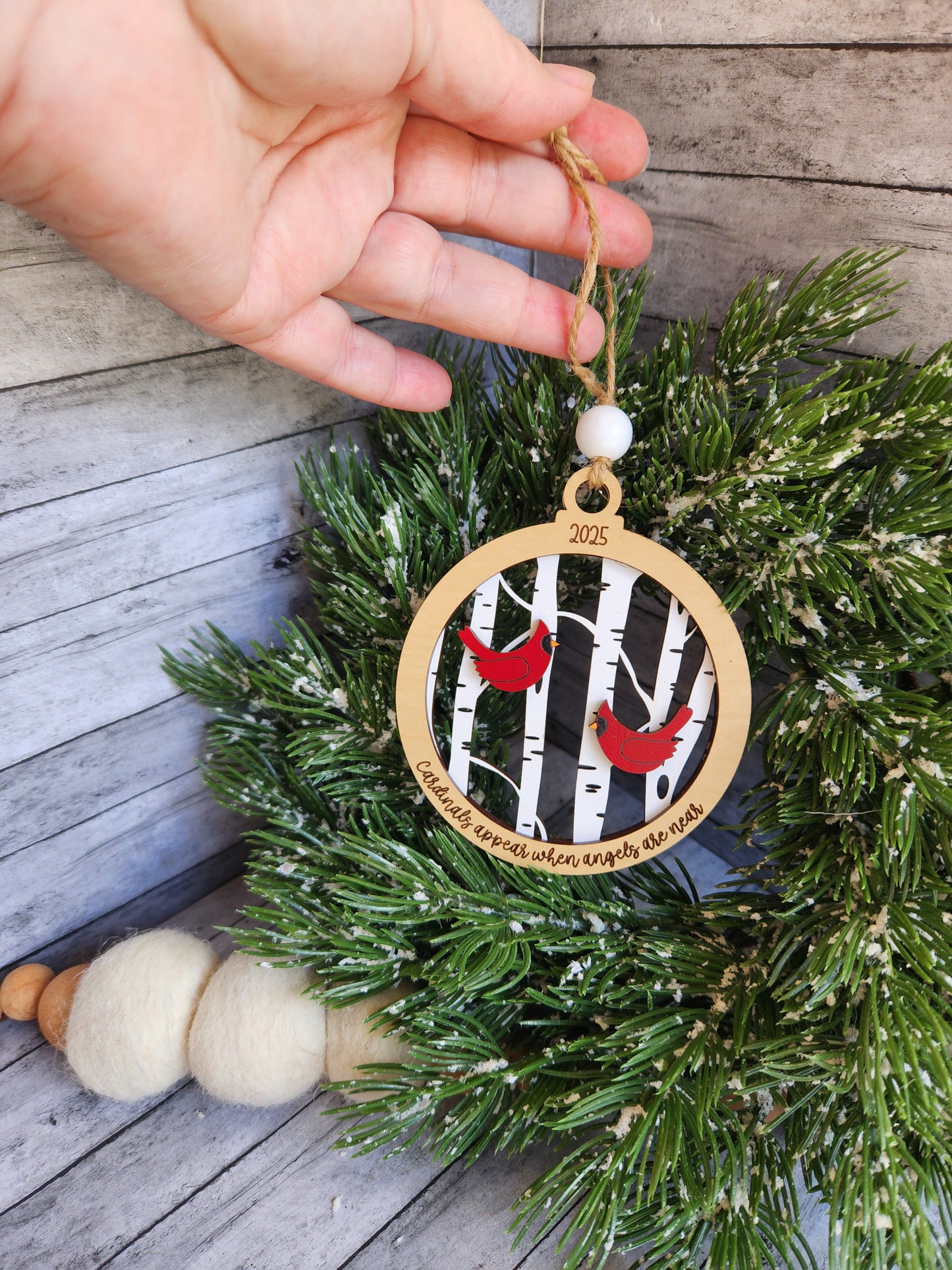 Hand holding a Christmas ornament with a measuring tape design on a wreath.