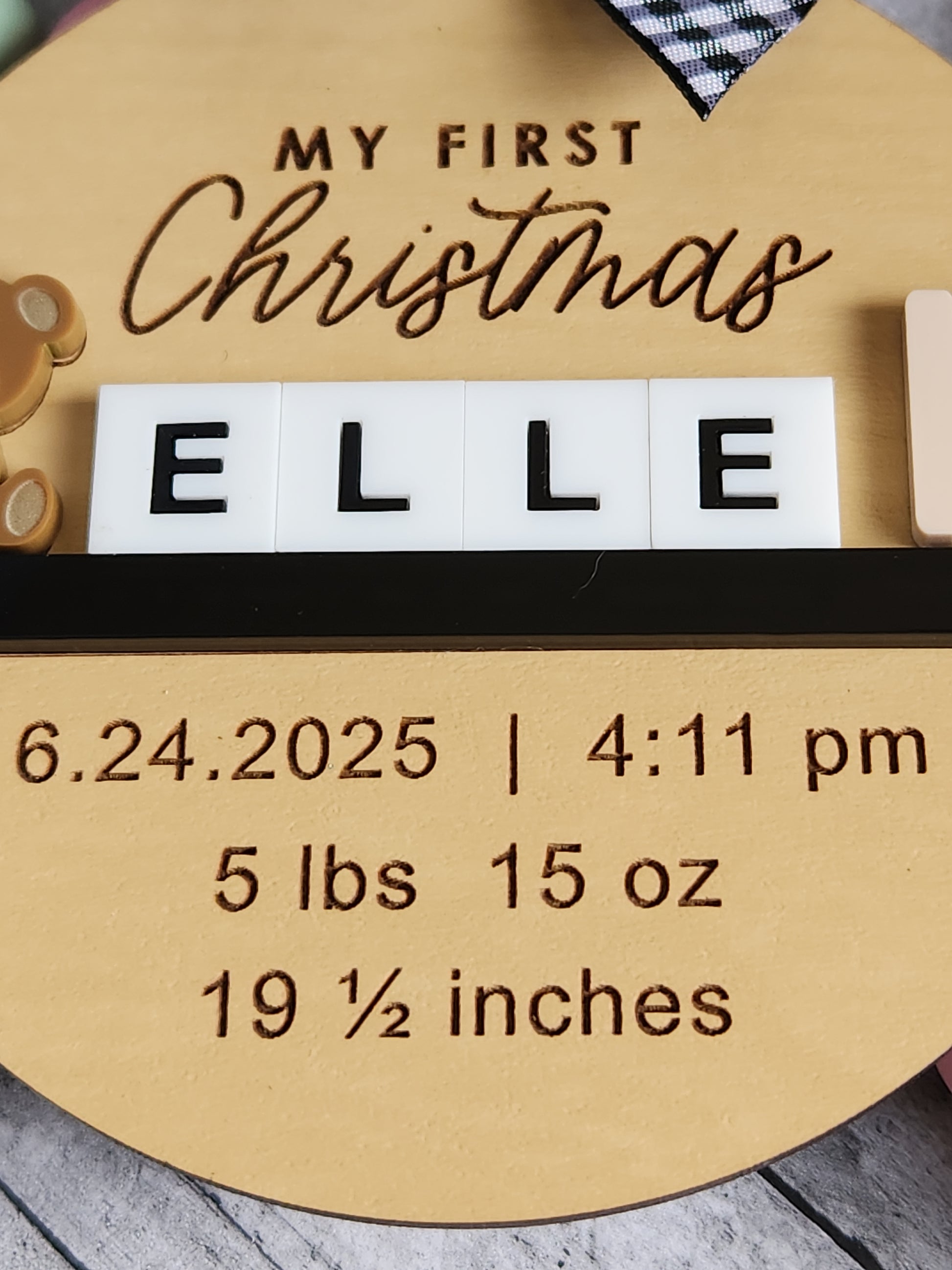 Wooden plaque with engraved text and baby blocks spelling 'ELLE' on a wooden background.