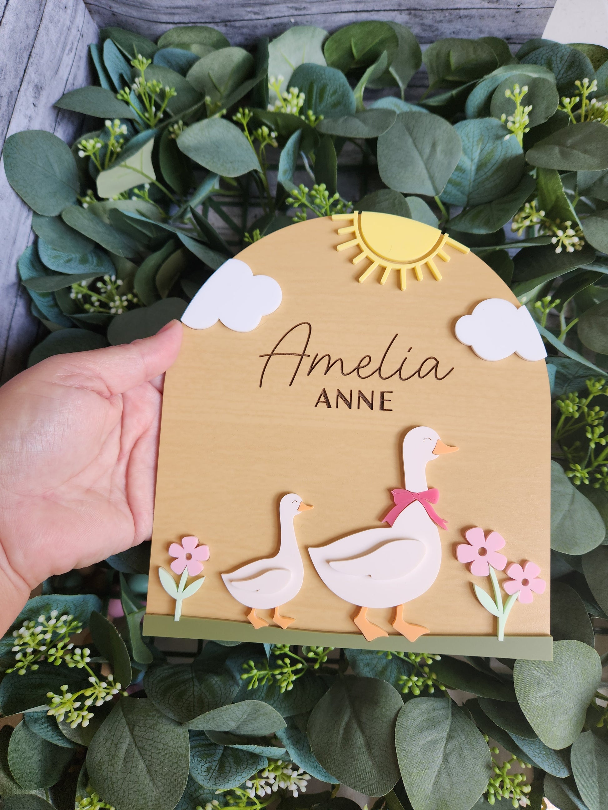 Hand holding a personalized card with decorative elements on a leafy background