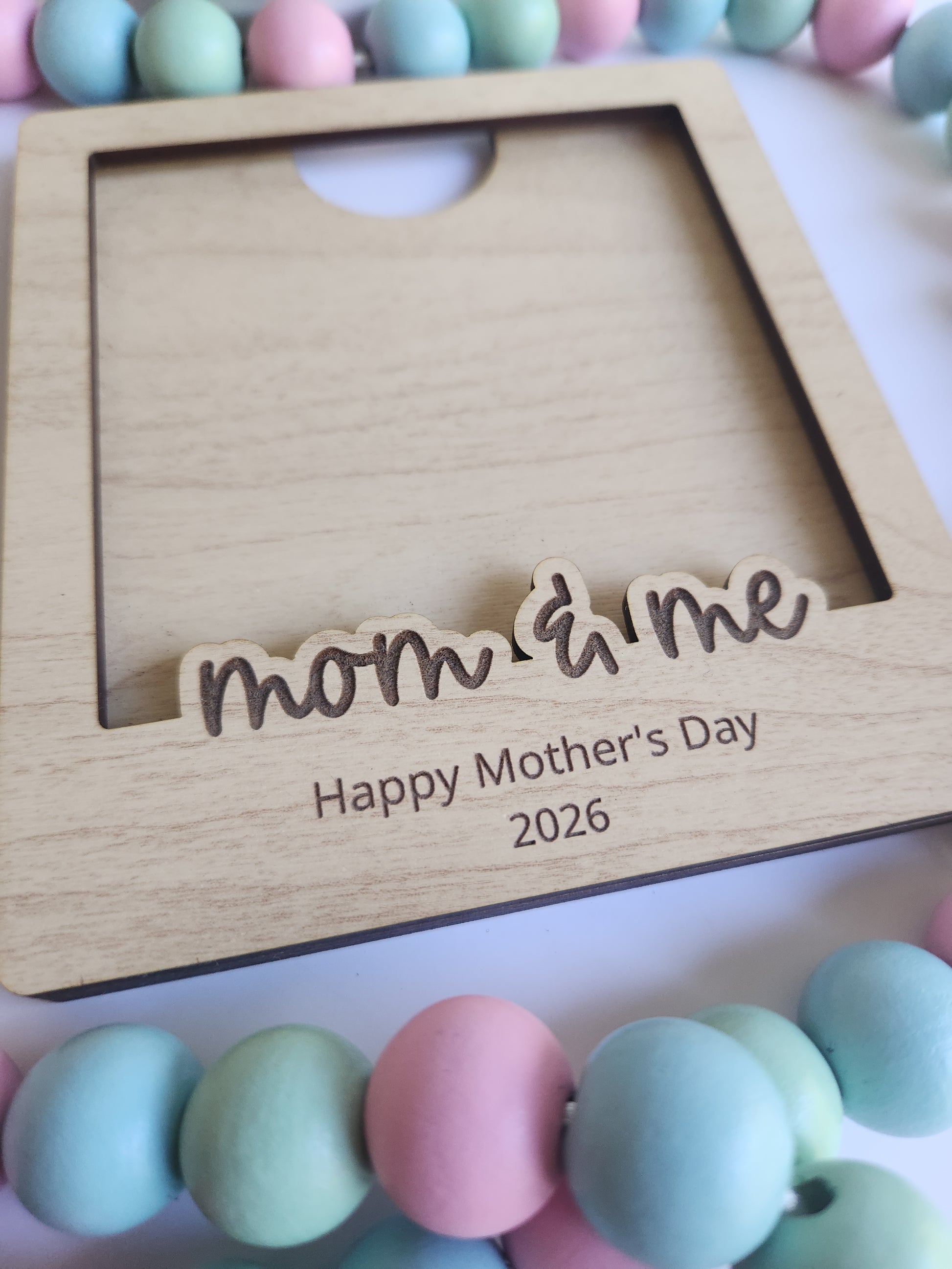 Wooden photo frame with 'mom & me' engraving and colorful beads in the background