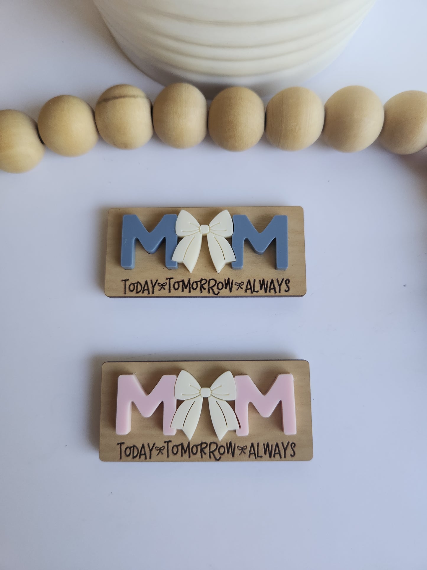 Two wooden blocks with colorful letters and flowers, next to a string of wooden beads on a white background.