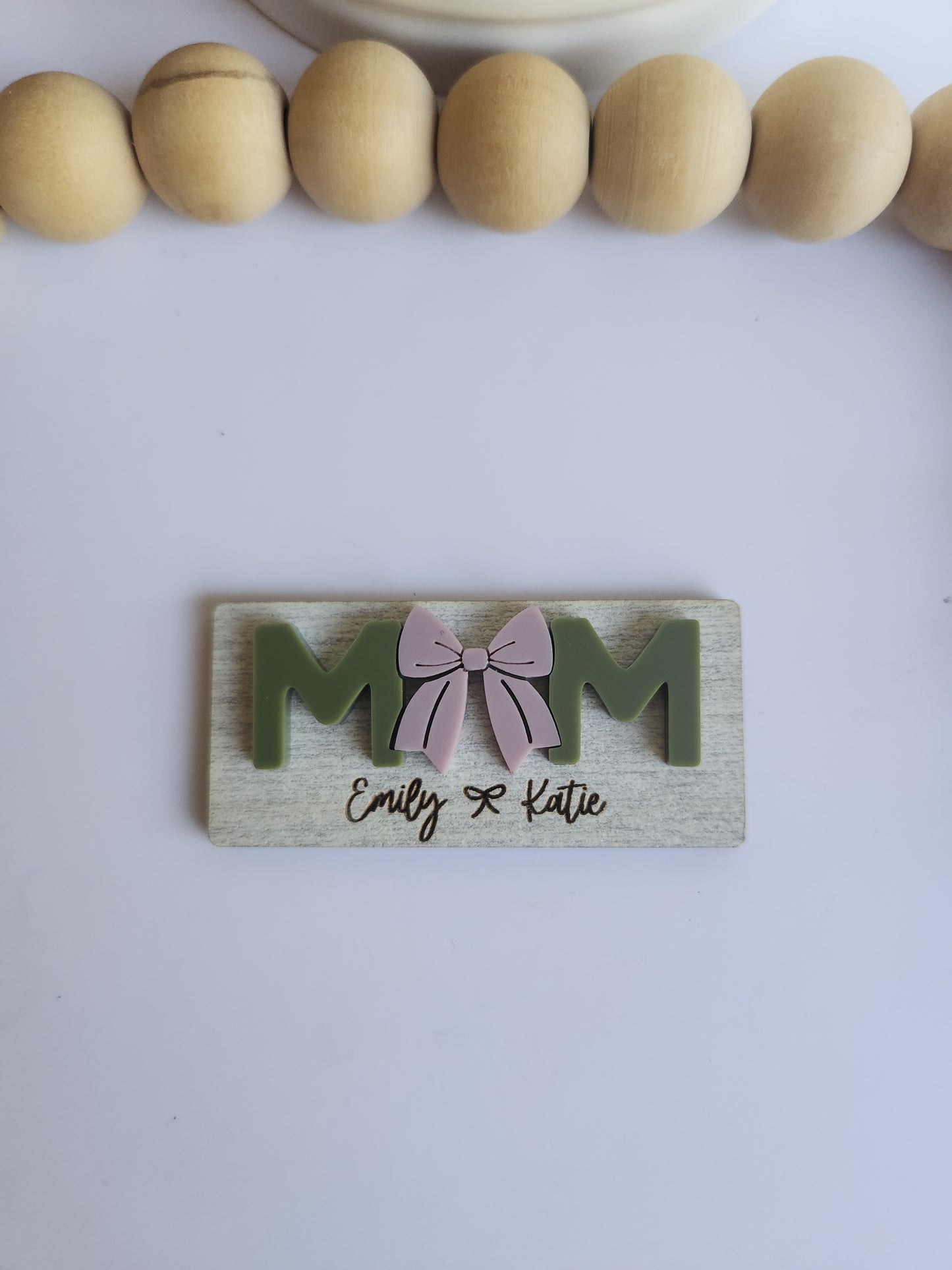 Wooden decorative item with 'MOM' and a bow design on a white background