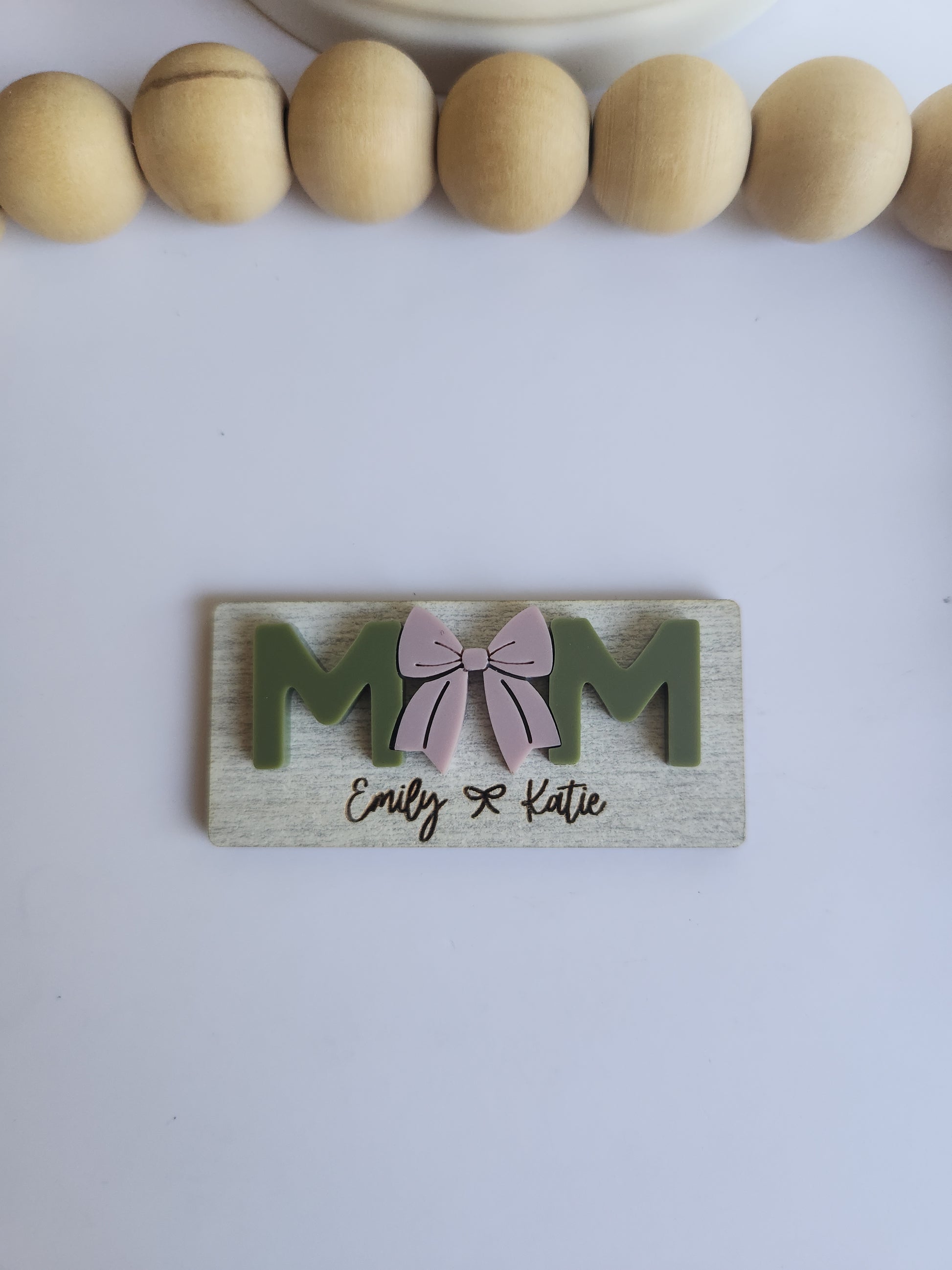 Wooden decorative item with 'MOM' and a bow design on a white background